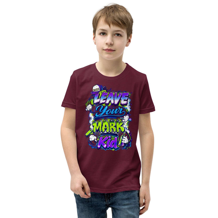 A young boy wearing a maroon t-shirt with a colorful graphic that reads 'LEAVE YOUR MARK Kid' in stylized purple, green, and white lettering, paired with blue jeans, set against a plain white background.