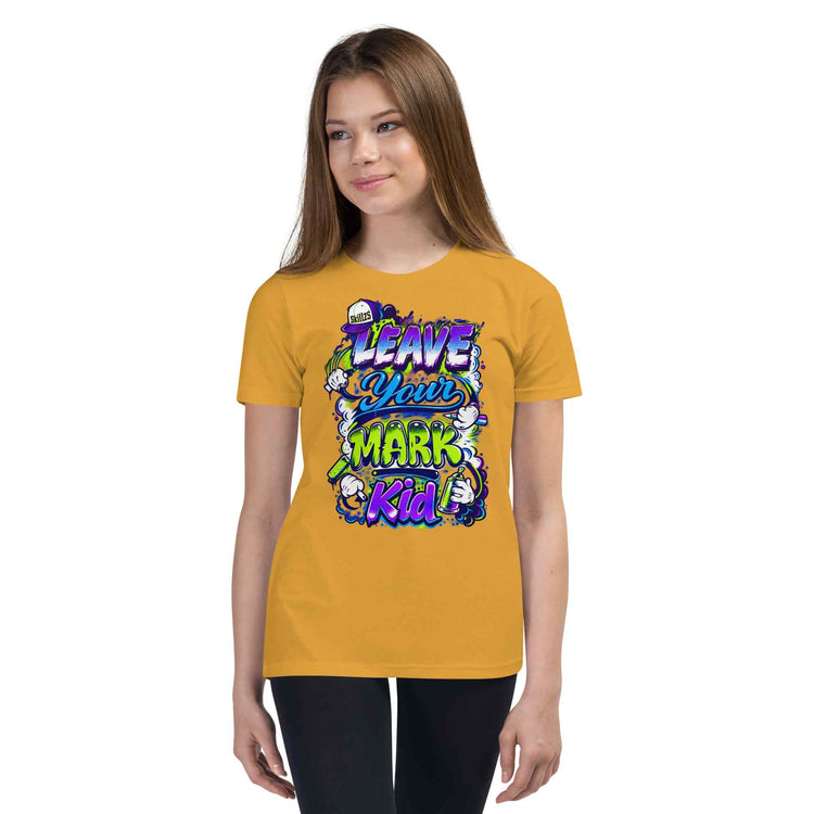A young woman modeling a mustard yellow t-shirt with a colorful graphic that reads 'LEAVE YOUR MARK Kid' in purple, green, and blue stylized lettering, set against a plain white background.