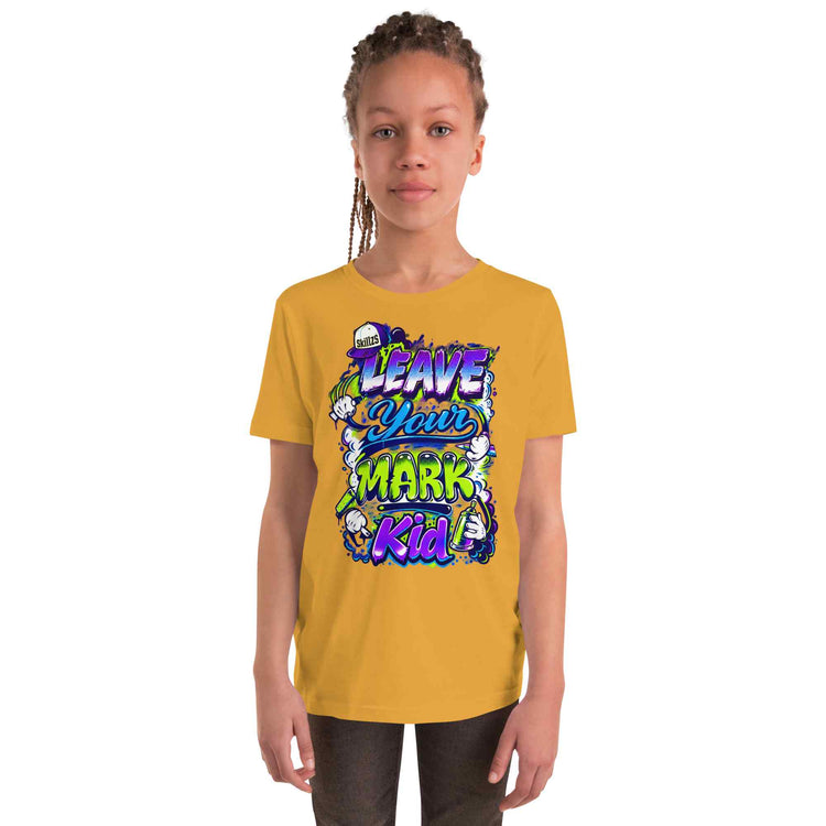 A young girl with braided hair wearing a mustard yellow t-shirt with a colorful graphic that reads 'LEAVE YOUR MARK KID'. She is standing against a solid white background.