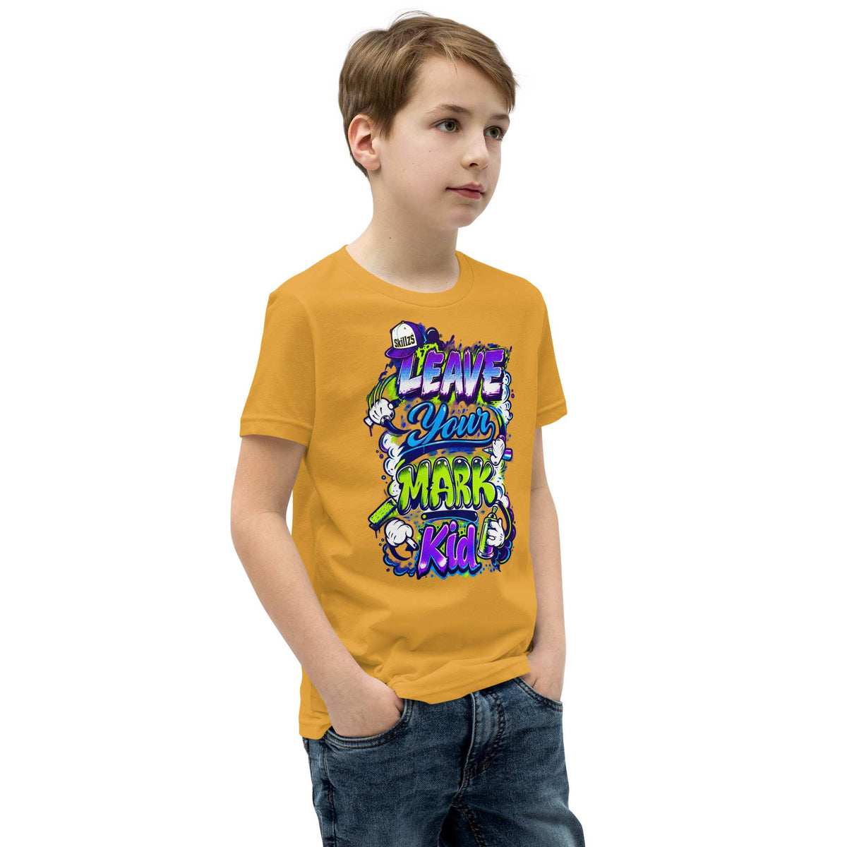 A young boy wearing a mustard yellow graphic t-shirt with a colorful cartoon design that reads 'LEAVE YOUR MARK Kid!', paired with blue jeans, set against a plain white background.