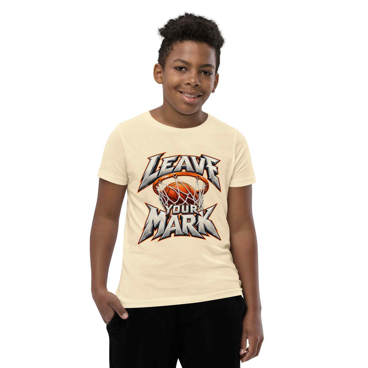 A young boy wearing a cream-colored t-shirt with a basketball-themed graphic that reads 'LEAVE YOUR MARK'. The background is solid white.
