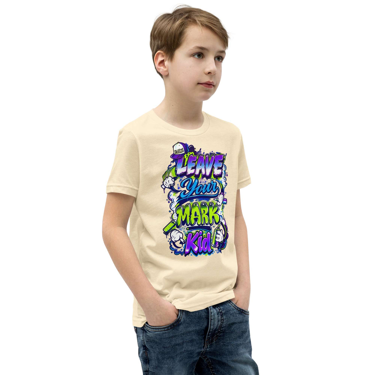 A child wearing a light beige graphic t-shirt with a colorful 'Leave Your Mark Kid!' design, paired with blue jeans, standing against a plain white background.