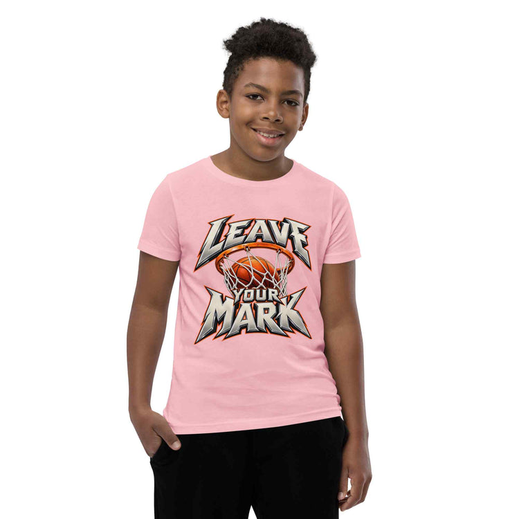 A child model wearing a light pink short-sleeve t-shirt with a 'LEAVE YOUR MARK' basketball graphic on the front, paired with black pants, set against a plain white background.