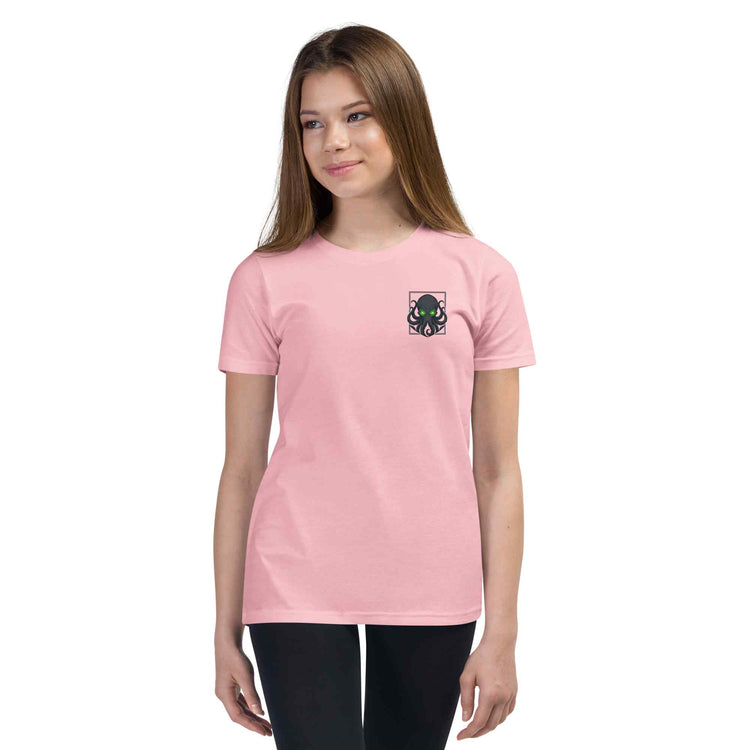 A young woman modeling a light pink short-sleeve crewneck t-shirt with a small kraken graphic on the left chest, set against a plain white background.