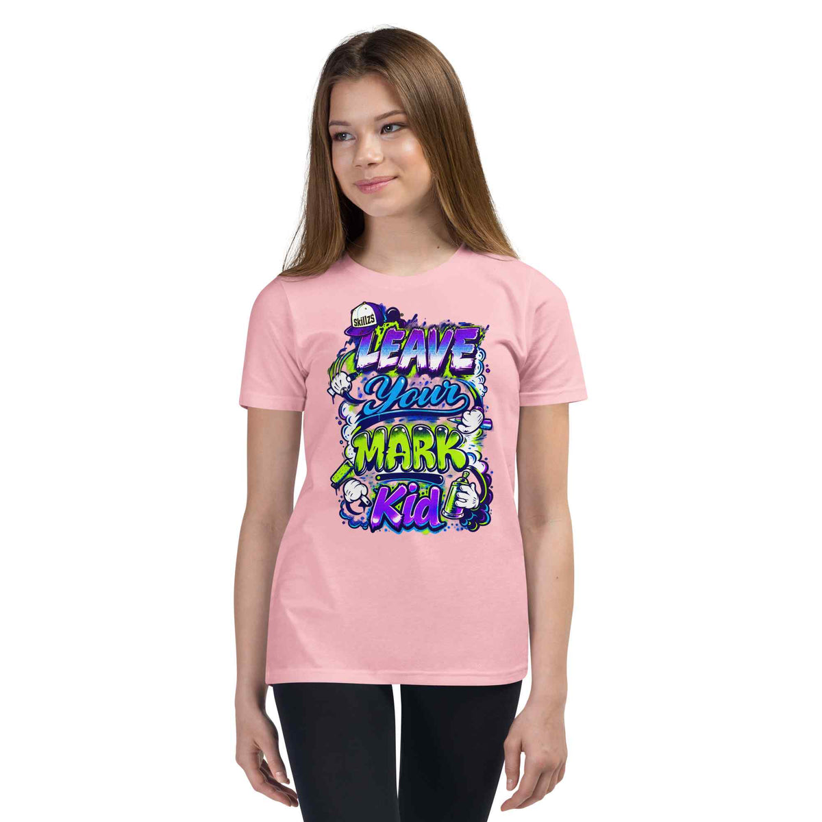 A young woman modeling a light pink t-shirt with a colorful graphic that reads 'LEAVE YOUR MARK Kid' in stylized purple, blue, and green lettering with cartoon characters, set against a plain white background.
