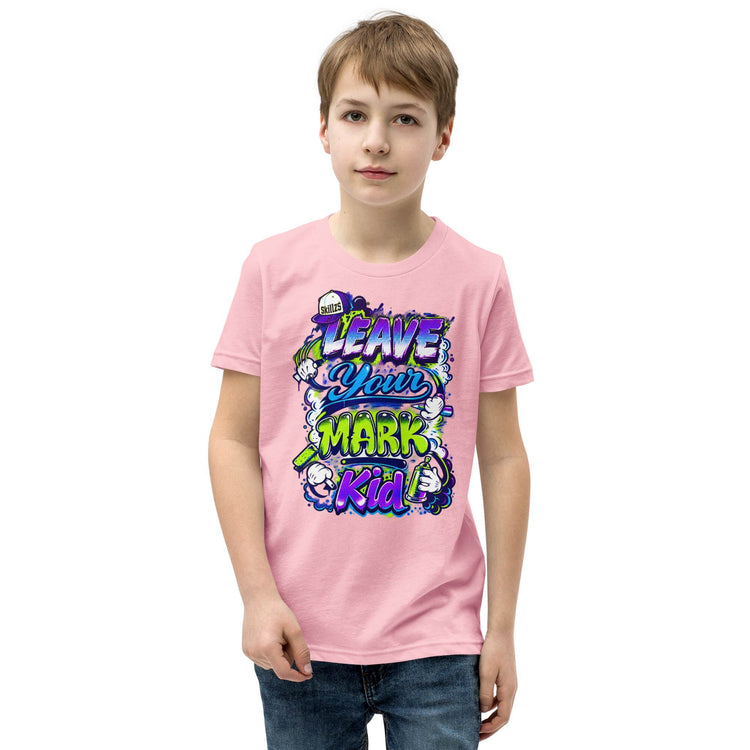 A young boy wearing a light pink t-shirt with a colorful graphic that reads 'LEAVE YOUR MARK Kid' in purple, blue, and green bubble letters, paired with blue jeans, set against a plain white background.