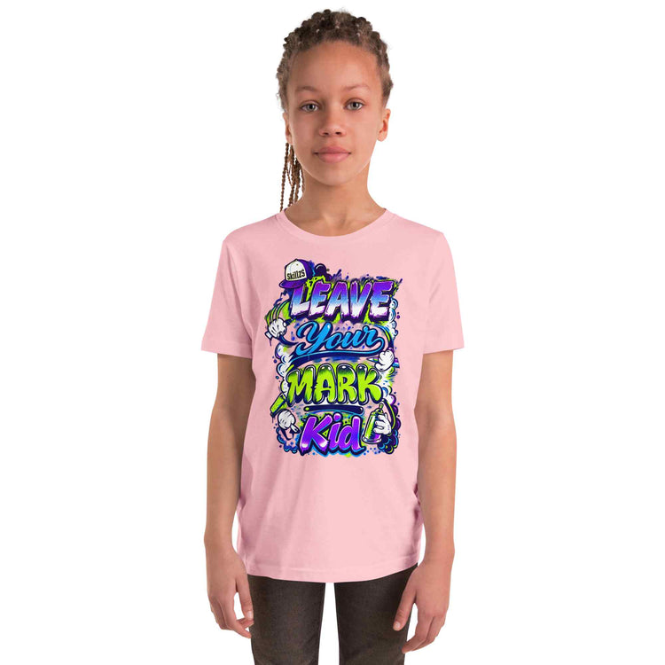 A young girl with braided hair wearing a light pink t-shirt with a colorful graphic that reads 'LEAVE YOUR MARK kid'. She is standing against a solid white background.