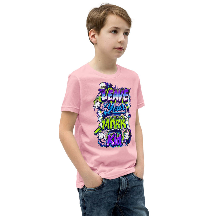 A young boy wearing a light pink t-shirt with a colorful graphic that reads 'LEAVE YOUR MARK Kid!' in stylized lettering, paired with dark blue jeans, set against a plain white background.