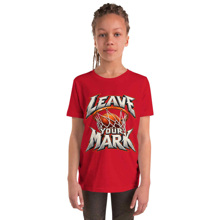 A young girl with braided hair wearing a red short-sleeve t-shirt with a 'LEAVE YOUR MARK' basketball graphic, standing against a plain white background.