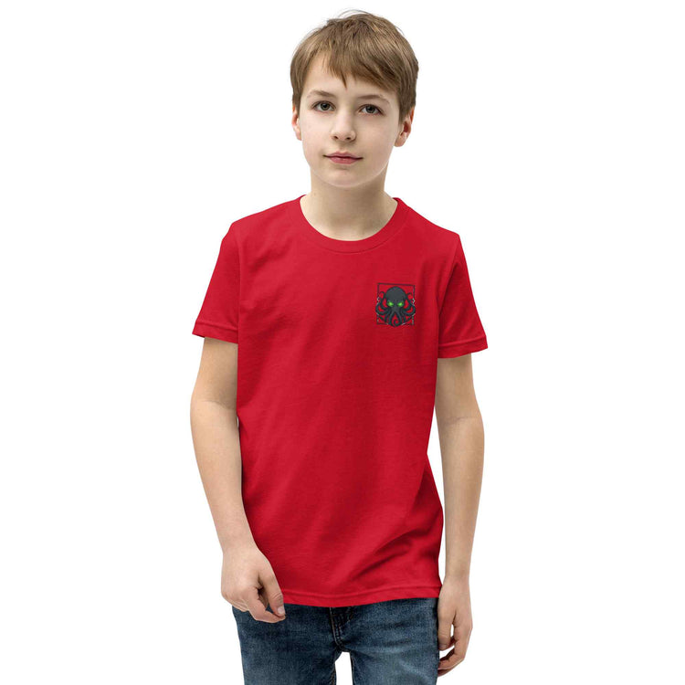 A young boy wearing a bright red short-sleeve t-shirt with a small Kraken graphic on the left chest, paired with blue jeans, photographed against a solid white background.