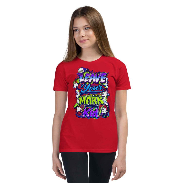 A young woman modeling a red short-sleeve t-shirt with a colorful graphic that reads 'LEAVE YOUR MARK Kid' in stylized purple, green, and white lettering with cartoon characters.