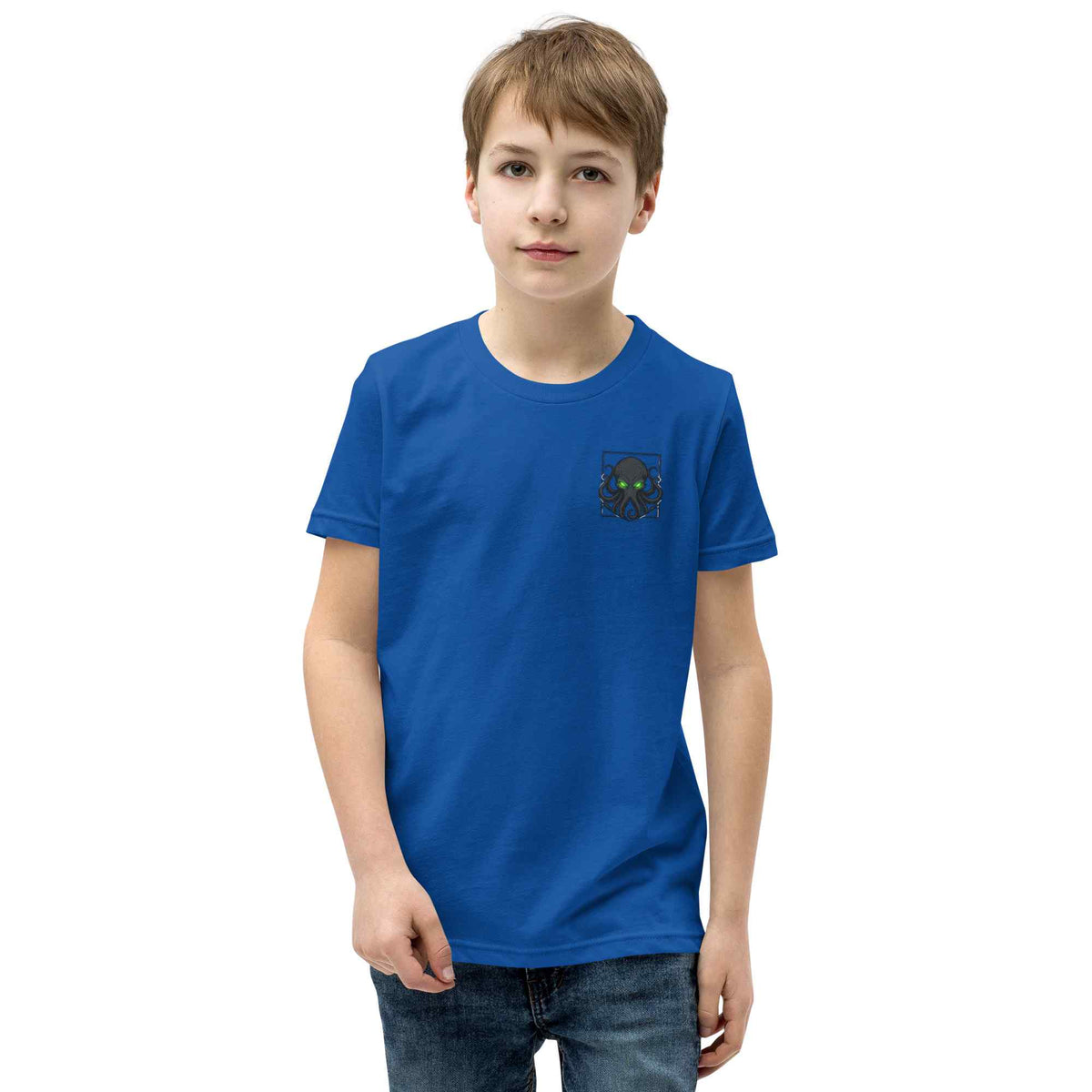 A young boy wearing a royal blue crewneck t-shirt with a small Kraken graphic on the left chest, paired with dark blue jeans, standing against a plain white background.