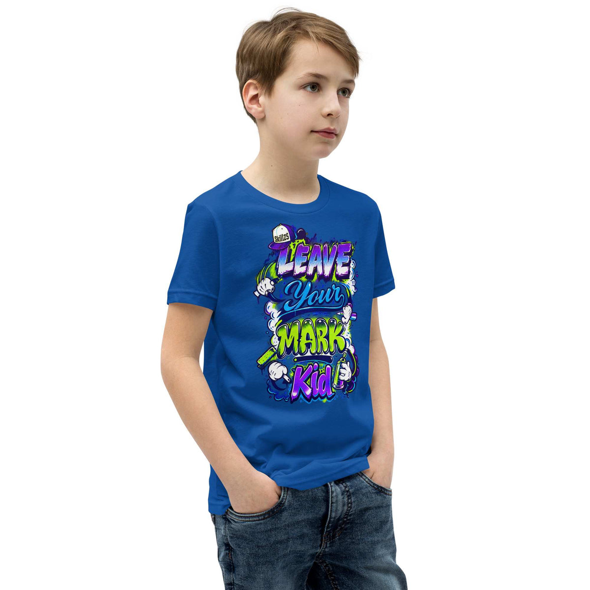 A young boy wearing a royal blue graphic t-shirt with the text 'LEAVE YOUR MARK KID!' in colorful cartoon-style lettering, paired with dark wash jeans, set against a plain white background.