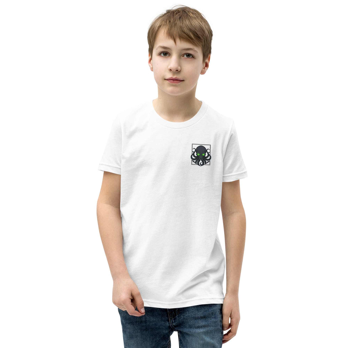 A young boy wearing a white short-sleeve crewneck t-shirt with a small kraken graphic on the left chest, paired with blue jeans, standing against a plain white background.