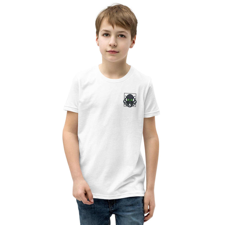 A young boy wearing a white short-sleeve crewneck t-shirt with a small kraken graphic on the left chest, paired with blue jeans, standing against a plain white background.