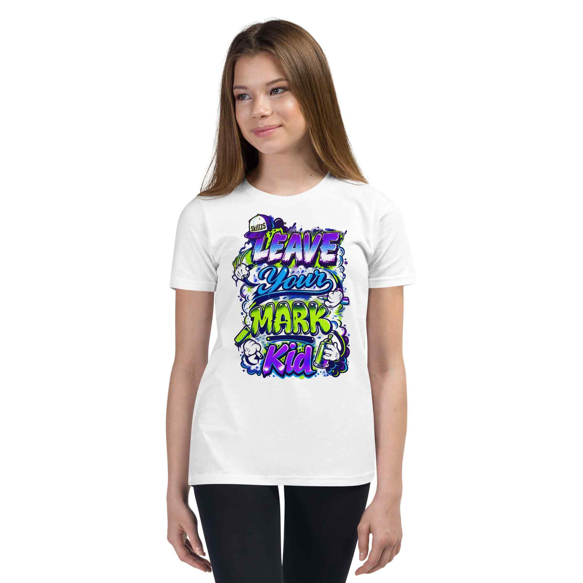 A young woman modeling a white short-sleeve t-shirt with a colorful graphic on the front that reads 'LEAVE YOUR MARK KID'. The graphic features a graffiti-style design with purple, green, and yellow text and cartoon elements.