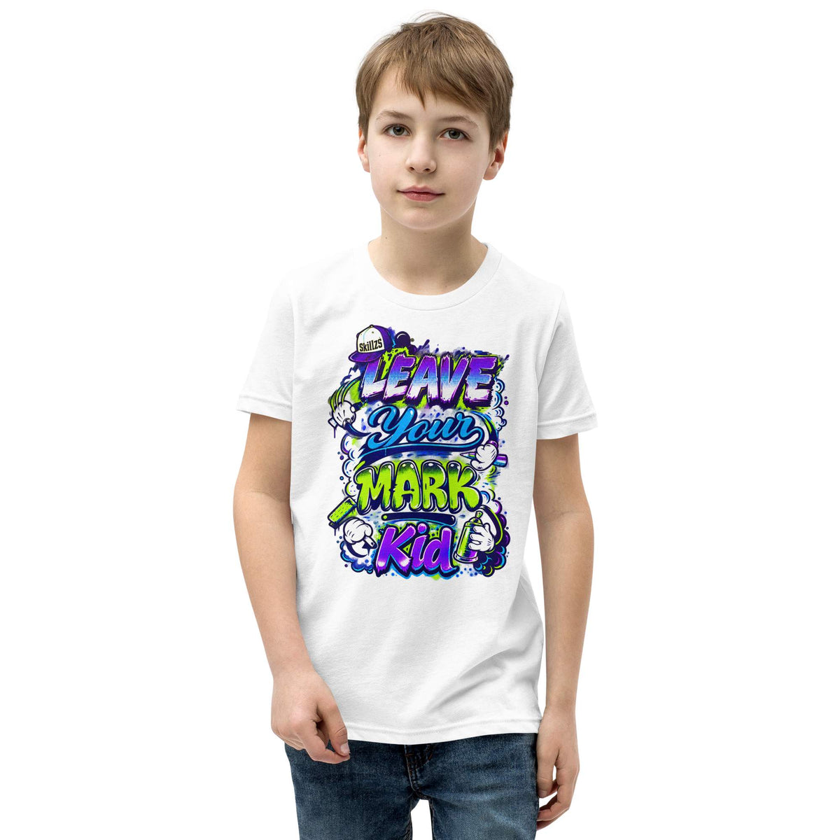 A young boy wearing a white crewneck t-shirt with a colorful graphic that reads 'LEAVE YOUR MARK KID' in purple, green, and blue stylized lettering, paired with blue jeans, set against a plain white background.