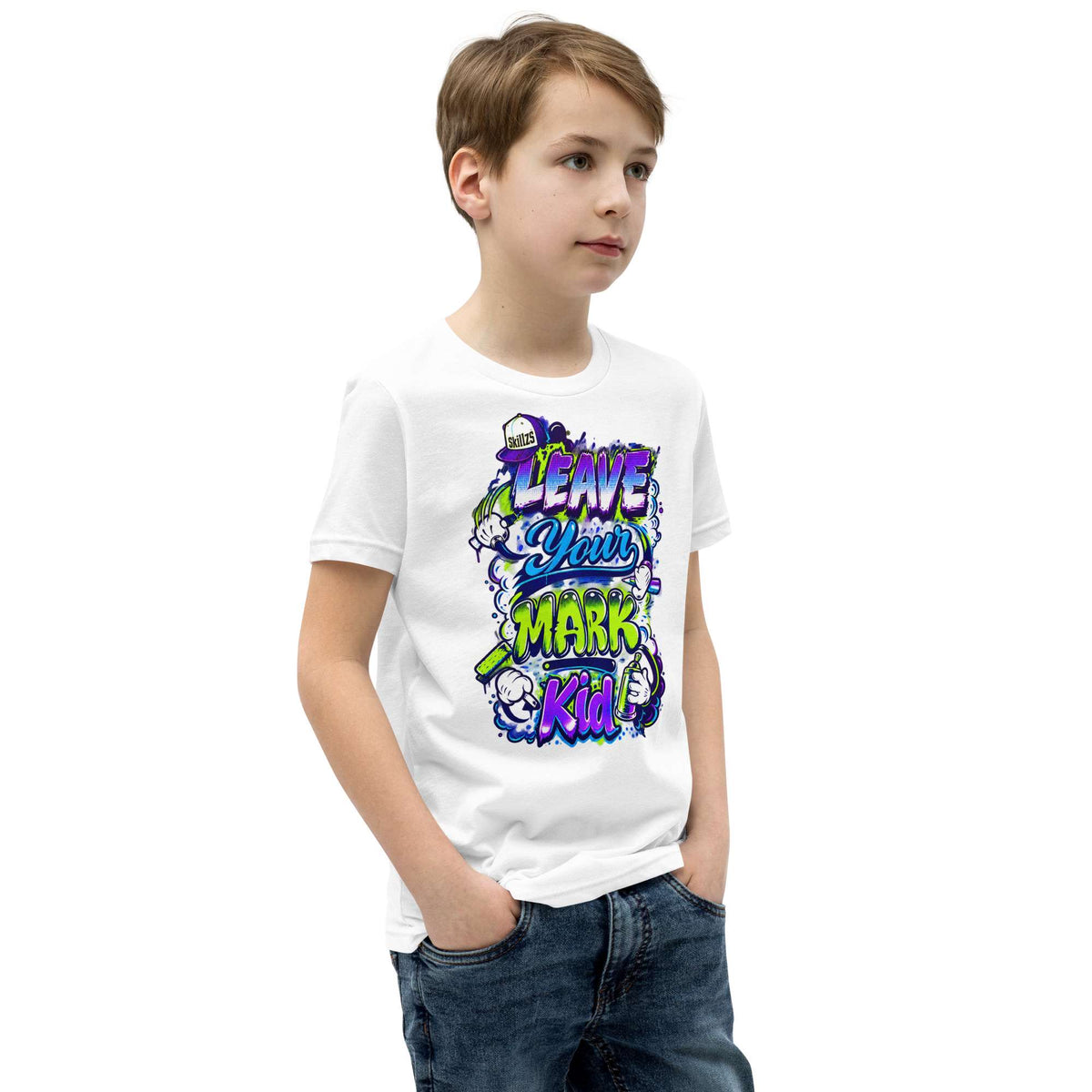 A young boy wearing a white short-sleeve graphic t-shirt with a colorful 'Leave Your Mark Kid!' design, paired with blue jeans, set against a plain white background.